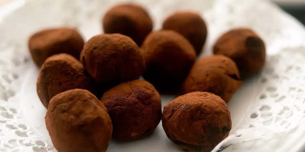 En hög med chokladtryfflar, pudrade med kakao, ligger på en vit spetsduk.
