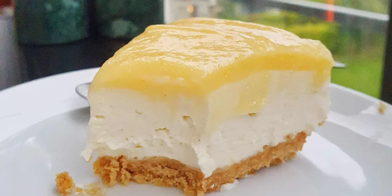 En bit krämig cheesecake med gul topping, perfekt för den som vill lära sig como hacer un cheesecake.