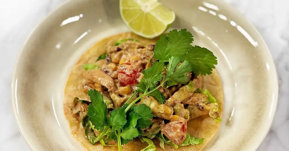 En läcker tostada de pollo med kyckling, majs, tomat och koriander, toppad med en limeklyfta.