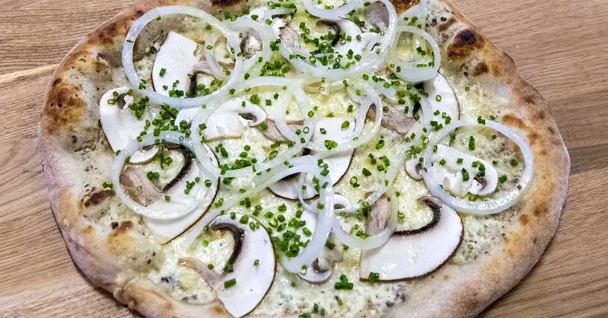 En pizza de hongos med tunna skivor champinjoner, lökringar och gräslök på en träbakgrund.