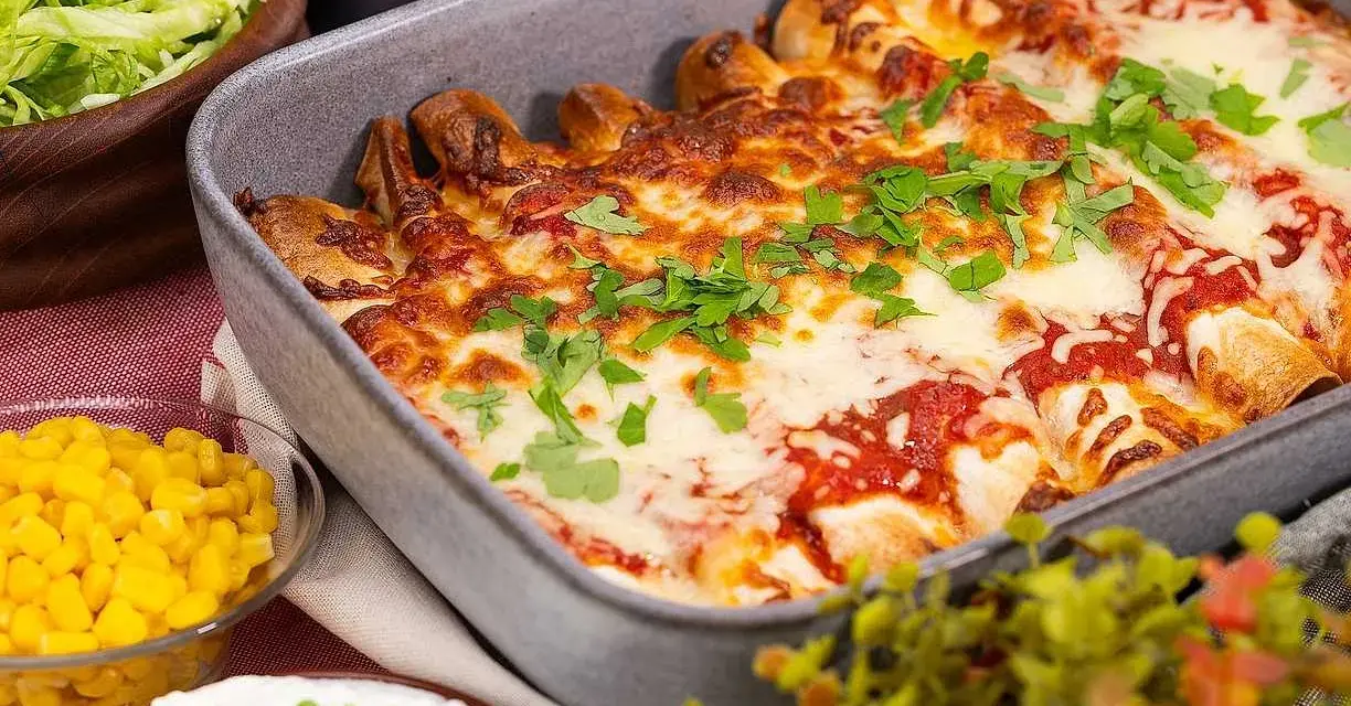 Enchiladas i ugnsform, toppade med smält ost och persilja. Tillbehör: majs, sallad och gräddfil. Perfekt för en middag med tortillas para enchiladas.
