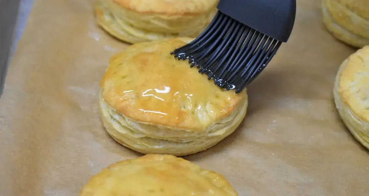 Pensel applicerar glansig glasyr på gyllene, flagnande pastelitos de carne.