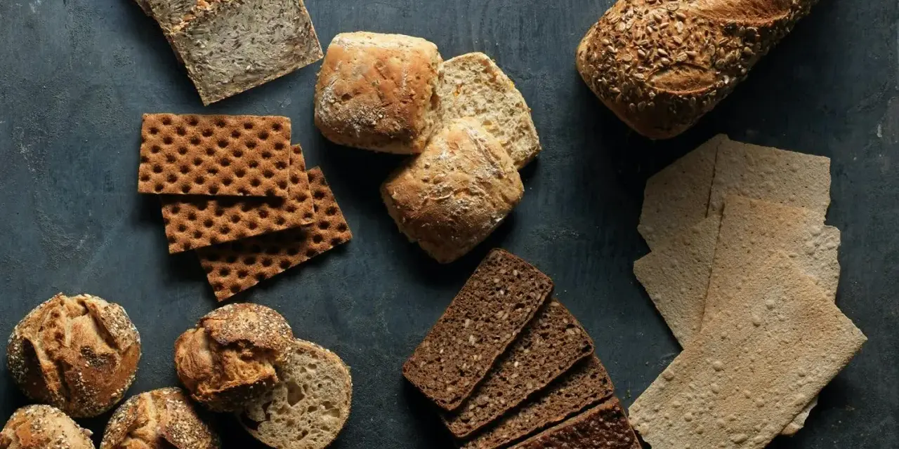 En variation av olika tipos de pan: mörkt rågbröd, knäckebröd, surdegsbröd och frallor.