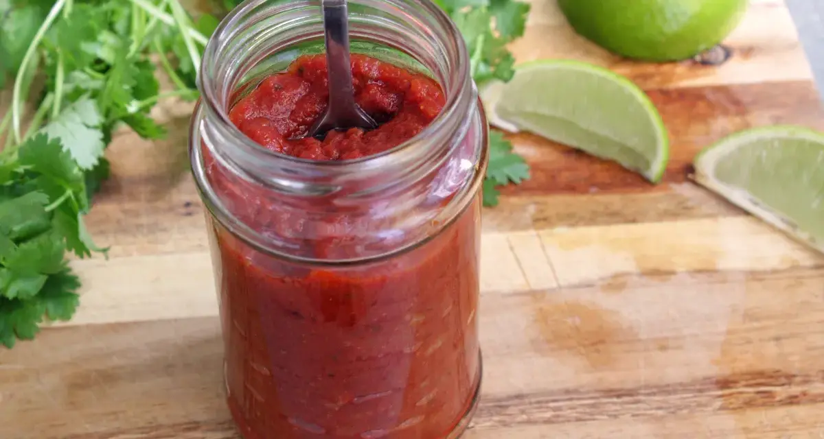En burk med hemlagad salsa para tacos, med färsk koriander och limeklyftor på en träskärbräda.