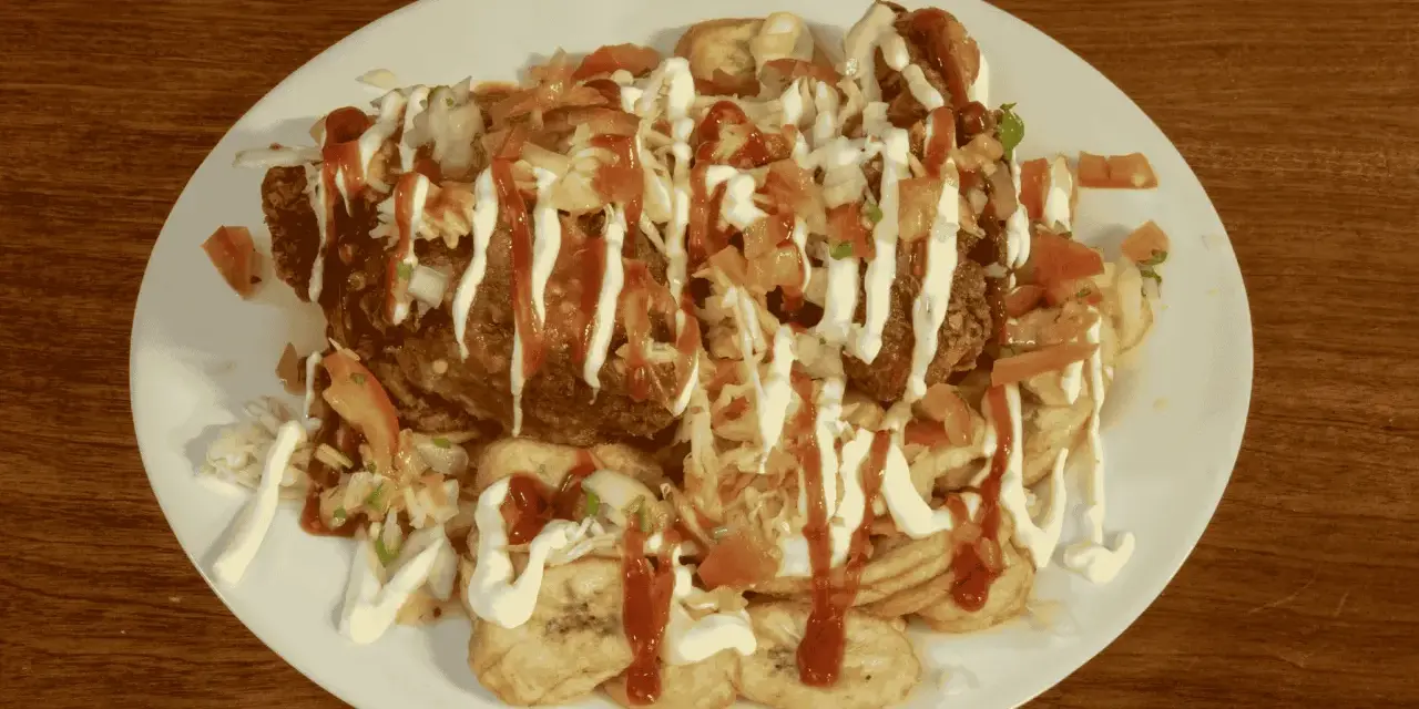 En tallrik med pollo chuco: friterad kyckling, stekta bananer, kål, tomat och majonnäs.