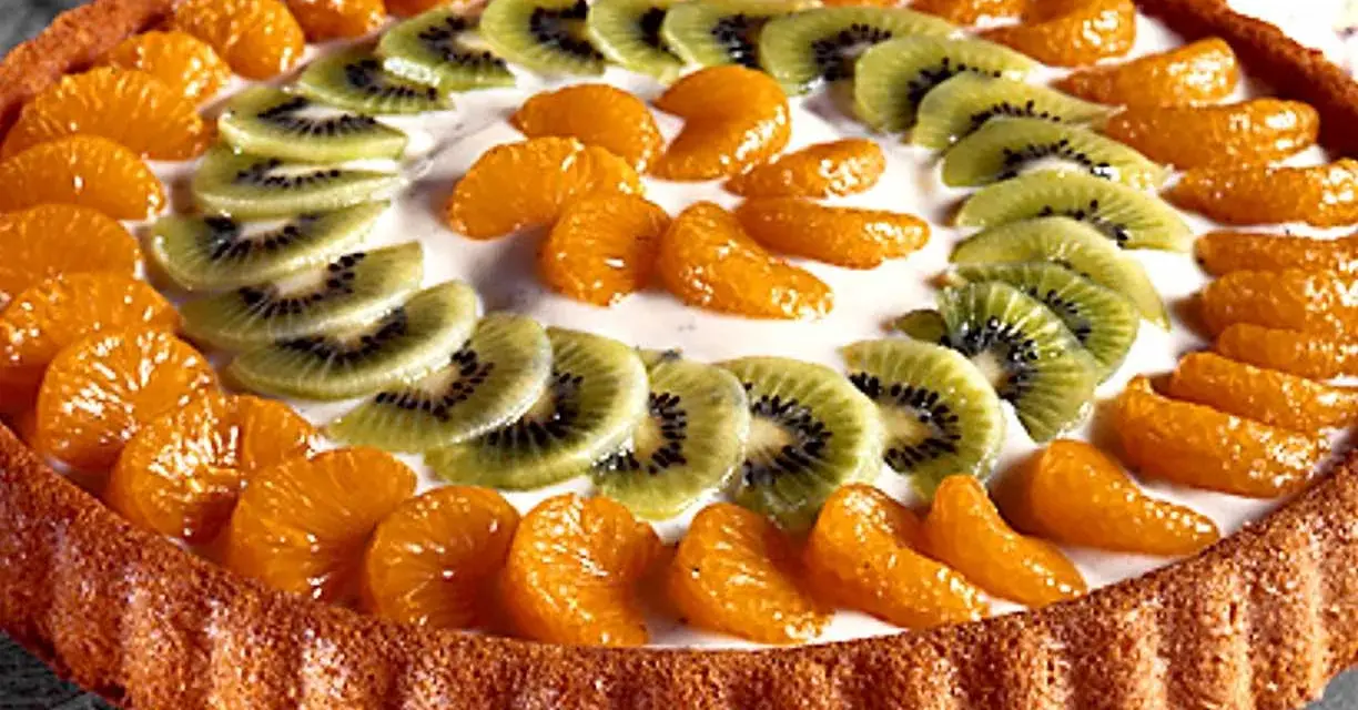 En vacker tartaleta de frutas med mandarinklyftor och kiwiskivor arrangerade i ett mönster på en krämig fyllning.