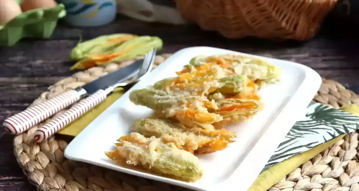 Friterade flor de calabaza på en vit tallrik, redo att avnjutas. Bredvid ligger en kniv och gaffel.