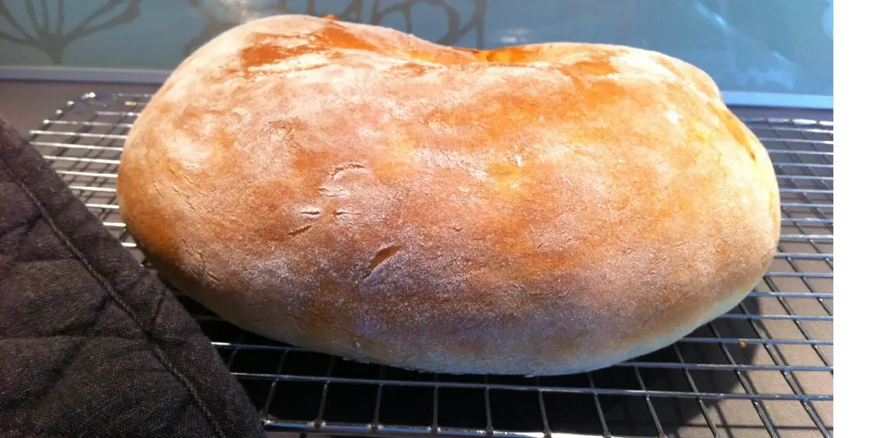 Ett nybakat, fluffigt **pan de torta** vilar på ett galler. En mörk grytlapp ligger bredvid.