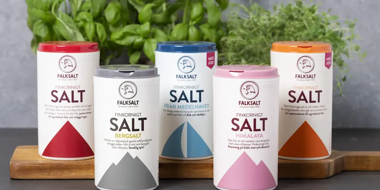 Fem olika tipos de sal från Falksalt: finkornigt, bergsalt, havssalt, Himalaya och jodberikat. Gröna örter i bakgrunden.