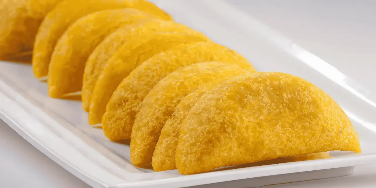 En rad gyllene empanadas de plátano ligger på en vit rektangulär bricka.