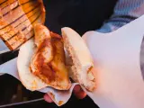 En hand håller en torta de tamal, en mexikansk smörgås med tamal inuti ett bröd, täckt med röd sås.