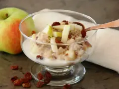 En skål med havregrynsgröt med äppelbitar och russin, bredvid ett äpple. Enkel guide för como preparar avena.