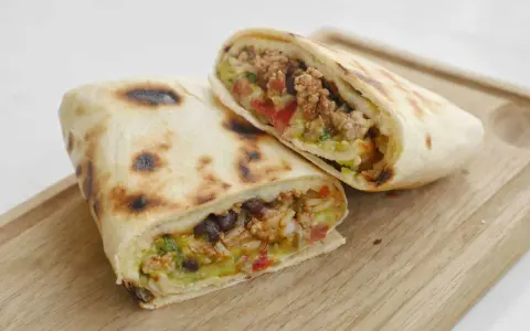 Två halverade burritos de carne med köttfärs, bönor, ris och grönsaker på en träskärbräda.