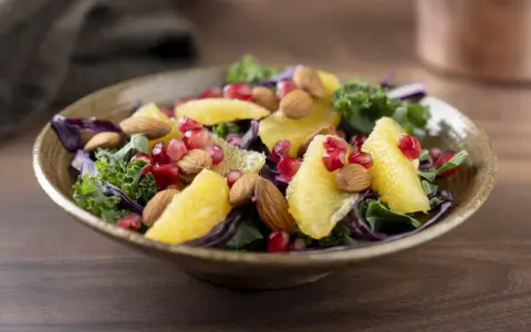 En färgstark sallad med apelsinklyftor, granatäppelkärnor, mandlar och olika typer av lechuga som grönkål och rödkål.