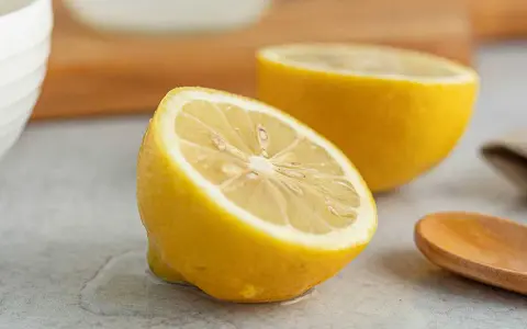 Två halvor av en saftig citron ligger på en grå yta. En träsked ligger bredvid. Perfekt för att pressa ut lite jugo de limón.