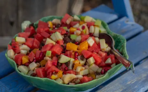 En stor skål med en färgglad ensalada de frutas, fylld med vattenmelon, äpple, apelsin, banan och granatäpple.