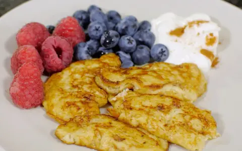 En tallrik med gyllene pannkakor, färska hallon, blåbär och en klick yoghurt med kanel. Perfekt för cenas para diabeticos.