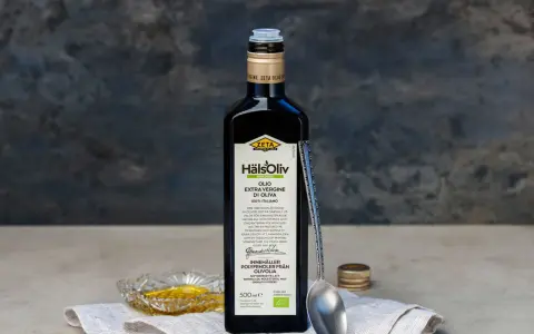 En flaska Zeta Hälsoliv Ekologisk Olio Extra Vergine di Oliva, perfekt aceite de oliva para cocinar. En sked och en liten skål med olja syns också.