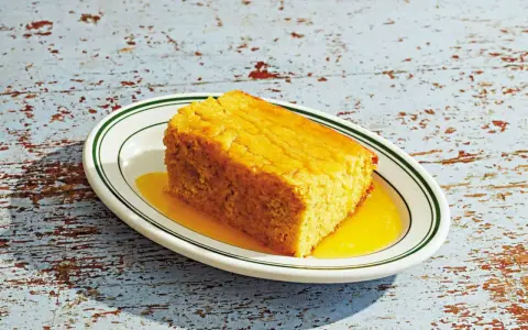 En bit gyllene pan de maiz, saftig och serverad med en gyllene sirap på en vit tallrik med gröna kanter.