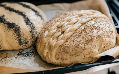 Två olika tipos de pan dulce, en med vallmofrön och en flätad med sesamfrön, redo att bakas.