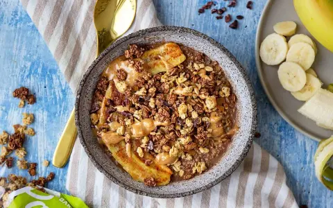 En skål med gröt, banan, granola och jordnötssmör. Perfekt för hälsosamma frukostar.