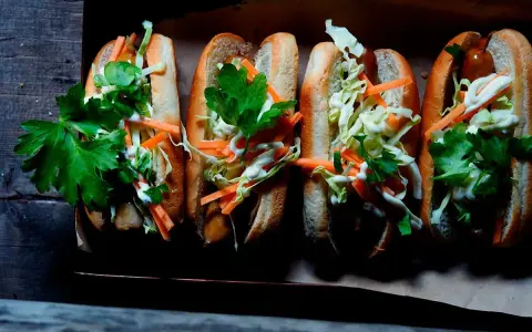 Fyra läckra korv med bröd, toppade med krispig kål, morötter och persilja. Enkel guide: como hacer un hot dog.