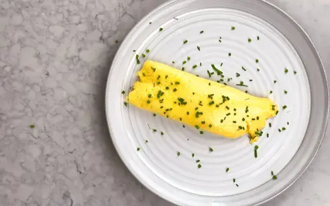 En perfekt rullad omelett, strödd med gräslök, på en tallrik. Enkel guide för como hacer un omelet.