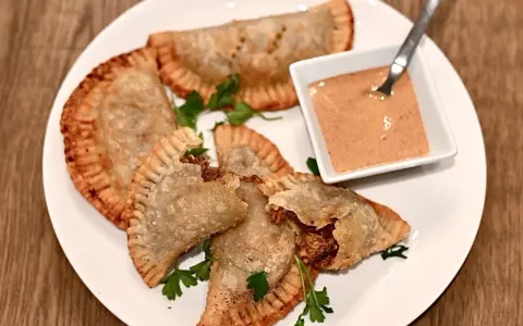 Friterade pastelitos de pollo med en krämig dippsås och persilja på en vit tallrik.