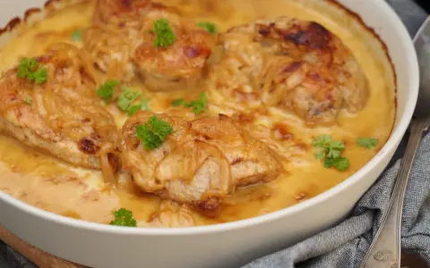 En ugnsform med saftig pollo encebollado salvadoreño, kyckling i en krämig löksås, garnerad med persilja.