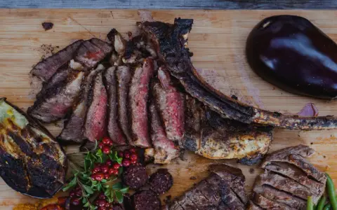 En saftig tomahawk steak, skuren i skivor, serveras med grillad aubergine, potatis i folie och lingon.