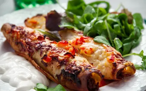 Två gyllene enchiladas, en typisk maträtt från Guatemala, serveras med en fräsch sallad och en klick gräddfil.