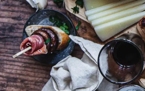 En läcker pinchos de carne med prosciutto, bröd och en skiva korv, serverad med ost och rödvin.