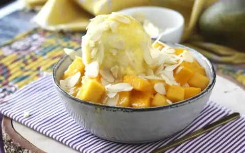 En skål med tärnad mango och en kula vaniljglass, toppad med mandelflagor. En härlig mango en miel-dessert.