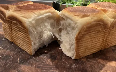 Mjukt och fluffigt **pan de leche** som brutits isär på en träskärbräda. Den gyllene skorpan kontrasterar mot det vita, trådiga inkråmet.