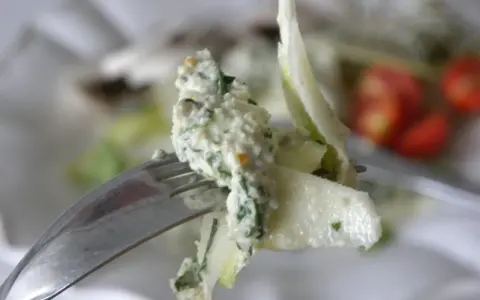 En gaffel med en krämig sallad, kanske med inslag av papayakärnor, nära körsbärstomater.