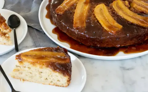 En saftig banankaka, en volteado de platano, med karamelliserade bananer på toppen. En bit serverad på en tallrik.