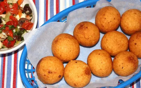Gylla gyllenbruna friterade bollar, som visar hur man gör buñuelos, i en blå korg. Bredvid en skål med en färgglad sallad.