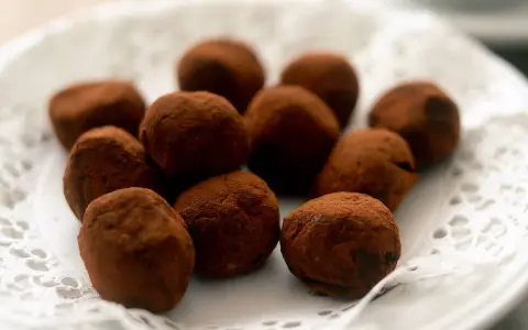 En hög med chokladtryfflar, pudrade med kakao, ligger på en vit spetsduk.