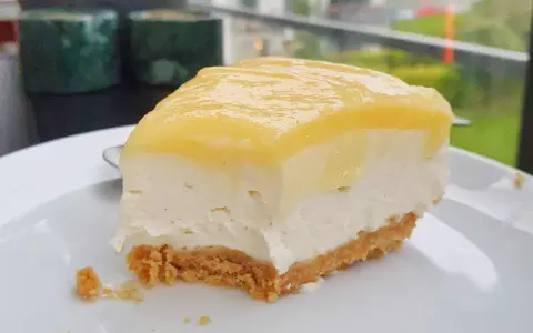 En bit krämig cheesecake med gul topping, perfekt för den som vill lära sig como hacer un cheesecake.