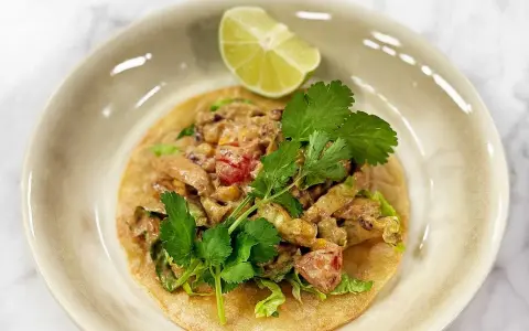 En läcker tostada de pollo med kyckling, majs, tomat och koriander, toppad med en limeklyfta.