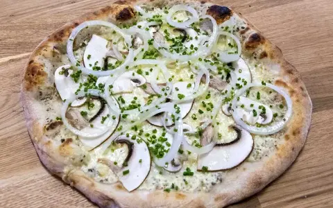 En pizza de hongos med tunna skivor champinjoner, lökringar och gräslök på en träbakgrund.