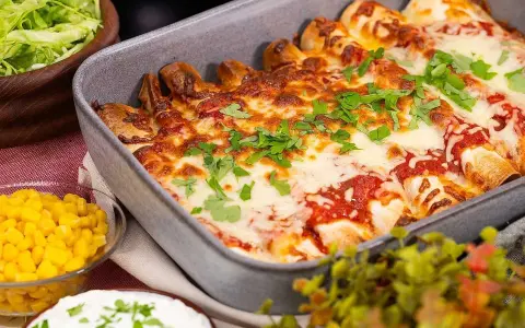 Enchiladas i ugnsform, toppade med smält ost och persilja. Tillbehör: majs, sallad och gräddfil. Perfekt för en middag med tortillas para enchiladas.