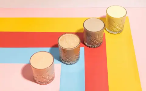 Fyra glas med olika **licuados para bajar de peso** står på en färgglad bakgrund i rött, gult, rosa och ljusblått.