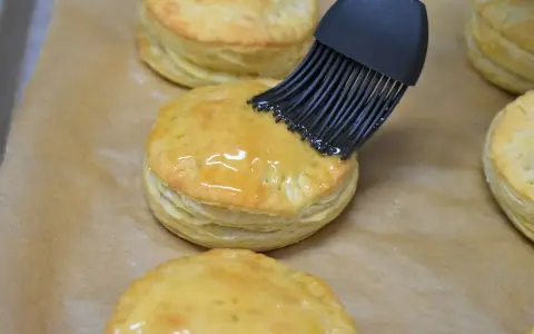 Pensel applicerar glansig glasyr på gyllene, flagnande pastelitos de carne.