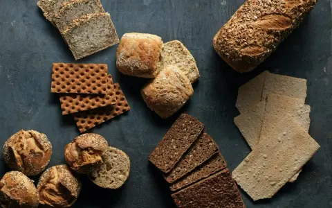 En variation av olika tipos de pan: mörkt rågbröd, knäckebröd, surdegsbröd och frallor.