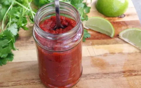 En burk med hemlagad salsa para tacos, med färsk koriander och limeklyftor på en träskärbräda.