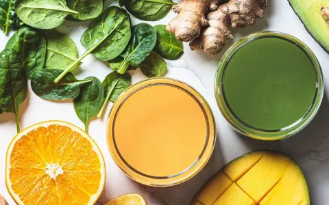 Färgglada juicer, en med apelsin och en grön, omgivna av färska ingredienser som spenat, ingefära, mango och avokado. Perfekt för en hälsosam "te de curcuma y jengibre"-inspirerad smoothie.