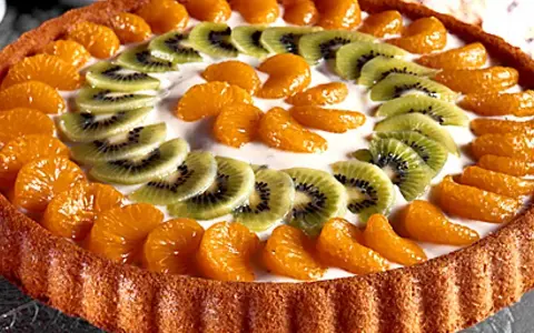 En vacker tartaleta de frutas med mandarinklyftor och kiwiskivor arrangerade i ett mönster på en krämig fyllning.
