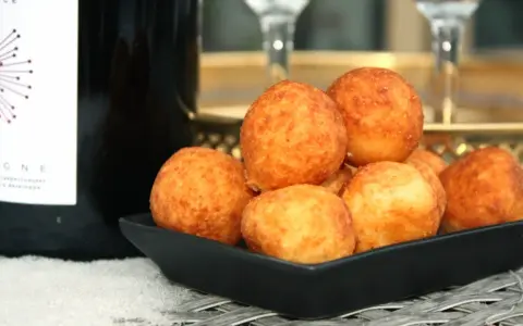 En svart skål fylld med gyllene pan de queso, bredvid en flaska champagne. Perfekt för en festlig stund.
