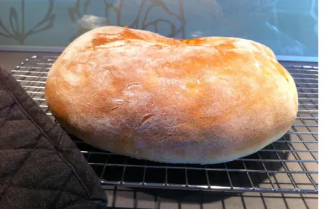 Ett nybakat, fluffigt **pan de torta** vilar på ett galler. En mörk grytlapp ligger bredvid.